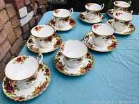 Seven Royal Albert Old Country Roses tea cups and saucers arranged on a blue cloth showing floral pattern and gold trim.