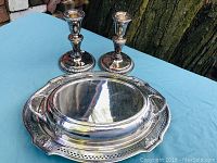 Silver plated tray, lidded serving dish, and two candlesticks arranged on a blue cloth outdoors showing full lot