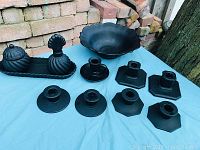 Overall view of black satin glassware pieces arranged on blue surface with brick background, showing lidded containers, bowl, candle holders and tray.