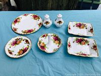 Set of Royal Albert Old Country Roses fine bone china pieces displayed on blue fabric, showing platter, divided dishes, and salt and pepper shakers.
