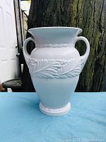 Front view of vintage Abingdon USA matte white pottery vase with leaf and vine embossed decoration and two side handles.