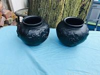 Pair of black satin glass vases with raised floral design shown outdoors on a light blue tablecloth in front of a tree.