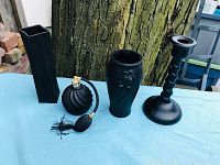 Photo showing all four black satin glass items on light blue cloth with tree background: square vase, round floral vase, perfume atomizer, candlestick holder.