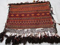 Photo showing one side of the Persian hand woven camel carry bag with geometric tribal patterns and woolen tassels bordering the piece.