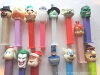 Front view of 14 PEZ dispensers showing character heads and colorful stems.