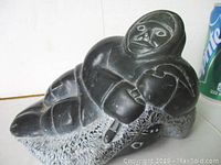 Front view of dark stone carving showing Inuit man holding seal, with detailed faces and textured seal fur.