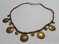 Photo of the full necklace laid flat showing the gold toned circular plates and small round bead charms along the chain.