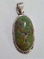 Front view of the sterling silver pendant showcasing the oval green stone with intricate inclusions and silver bezel setting.