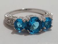 Front view showing three round blue topaz-like stones set in a sterling silver ring with milgrain detail on the band.