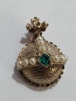 Front view of vintage brooch showing metal round base, crown detail, pearls arranged in cross pattern and central green stone.