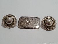Three pieces: one rectangular engraved brooch and two circular earrings with decorative edges, all sterling silver.