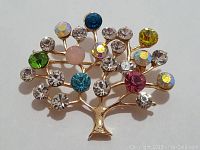 Front view of the gold-toned tree-shaped brooch with multi-coloured crystal stones showing details of the stones and metal frame.