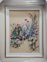 Framed acrylic painting showing a colorful garden scene with multiple flowers and plants, signed by the artist.