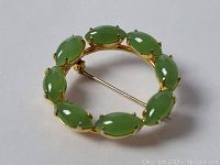 Front and back views of the circular brooch showing nine green jade stones set in 12k gold metal frame with pin clasp.