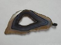 Close-up photo of the triangular layered natural stone pendant showing color bands and hollow center with crystals.