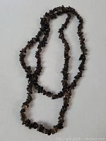 Full view of the garnet bead necklace laid in a looped fashion on a white background, showing overall length and bead irregularity.