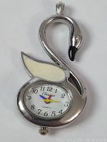 Front view of the silver-toned swan-shaped pendant watch, showing the white wing inlay and the watch face with black numerals and colored hands.