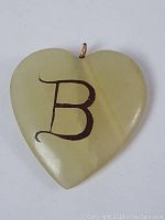 Heart-shaped pale green Connemara marble pendant with a black initial 'B' inscribed on one side and a metal hanging loop.