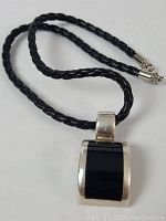 Full view of black braided leather necklace with sterling silver framed black onyx pendant.