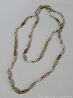 Full view of the long necklace showing the variety of jasper stones in different colors like green, purple, brown and cream, spaced with knots.