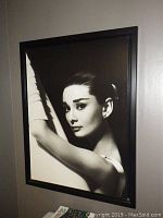 Framed black and white photographic print of Audrey Hepburn shown hanging on wall in close-up detail.