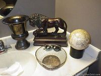 Photo showing the bathroom countertop with a bronze or brass vase, resin lion statue, vintage-style globe, and metal wire basket.