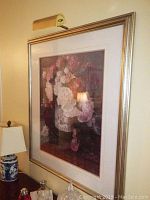 Floral print in silver-tone frame with white and pink matting hung on wall, overhead light attached.