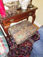 View of the wooden side table with glass top and upholstered ottoman, showing drawer and overall condition.