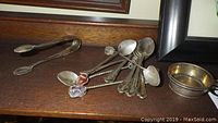 Overview of sterling silver spoons, sugar tongs, and salt dish with visible tarnish and twisting detail on spoons.