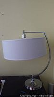 Full view of the lamp showing the metal base and fabric shade against a light wall background