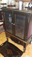 Front view of wood bar cabinet showing two glass doors with metal knobs and gold trim details