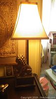 Lamp lit showing cream fabric shade and composite lion base on black pedestal