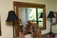 Framed mirror hanging on wall reflecting window and objects in room, showing size and surrounding environment.