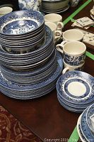Stack of blue and white transferware plates, bowls and cups displayed on table