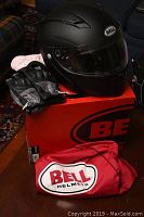 Full view of Bell Revolver Eve helmet in matte black with clear visor, placed on red Bell box with gloves and helmet bag.