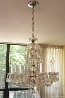 Full view of chandelier hanging from ceiling, showing eight lights and crystal strands