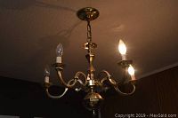 Full view of brass finish chandelier hanging from ceiling with five lit candle-shaped bulbs