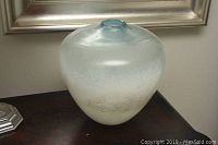 Front and side view of the glass art vase showing its round bulbous form, frosted finish, small opening, and light blue tint.