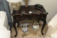 Full view of vintage side table showing scalloped and slightly curved top, drawer with two handles, and cabriole legs.