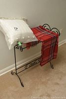 Metal blanket stand holding a white decorative pillow and a red plaid throw blanket.