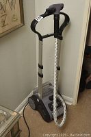 Full view of the Rowenta clothes steamer showing upright handle, braided steam hose coiled around it, and wheels.
