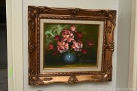 Front view of framed floral oil painting showing bouquet of pink and red flowers in blue vase, ornate gold frame with detailed carving.