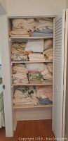 Four shelves in a closet holding folded linens, towels, blankets and bedding in various colors and patterns.
