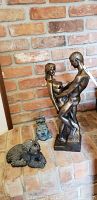 Three items grouped on floor: bronze nude couple sculpture, blue-green partial bust, and Sandicast dog figurine with chips