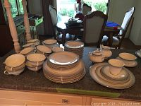 Wide shot of all china pieces on counter including stacked plates, bowls, cups, cream and sugar containers.