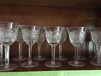 Close up view of 8 American Brilliant Cut crystal wine glasses with Monarch-like geometric and floral cut pattern, displayed on wooden shelf