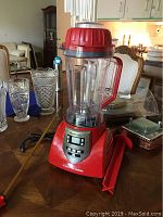 Red HealthMaster Elite blender with clear pitcher and red lid, digital control panel.