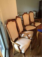 Set of four wooden dining chairs, three captain's chairs with armrests and one side chair without armrests, all upholstered in beige patterned fabric.
