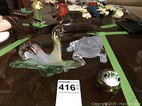 Overview showing Murano swan, Lalique frog, painted frog figurine, metal flower sculptures and wooden shark carving on table