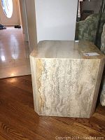 Side view of cube-shaped travertine marble end table on hardwood floor showing natural stone patterns and texture.